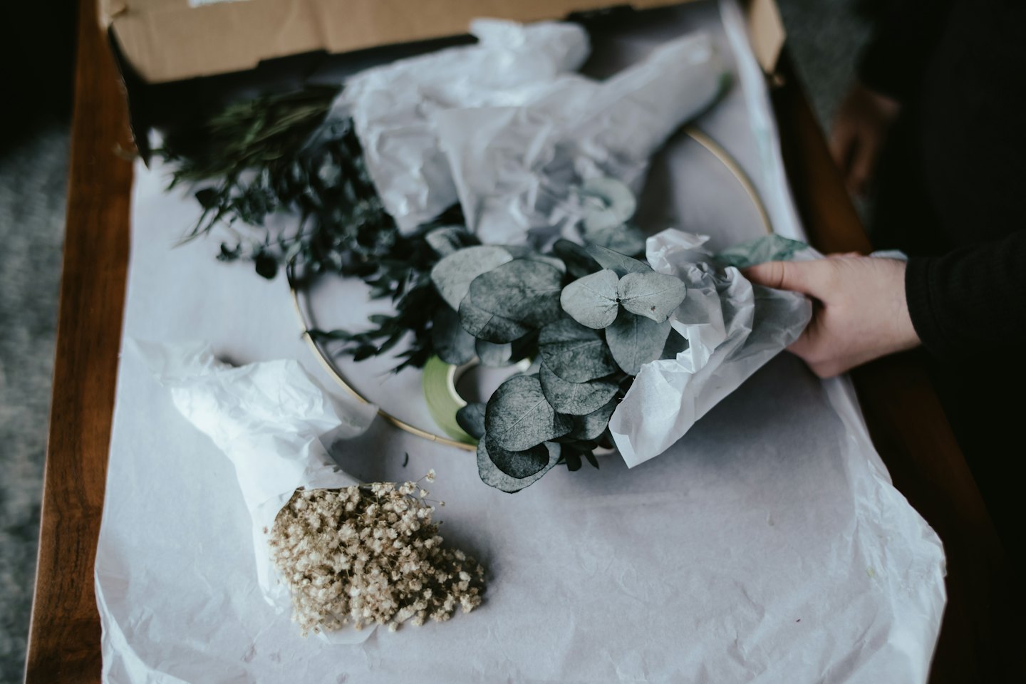 Hands arrange foliage and a brass hoop inside a gift box.