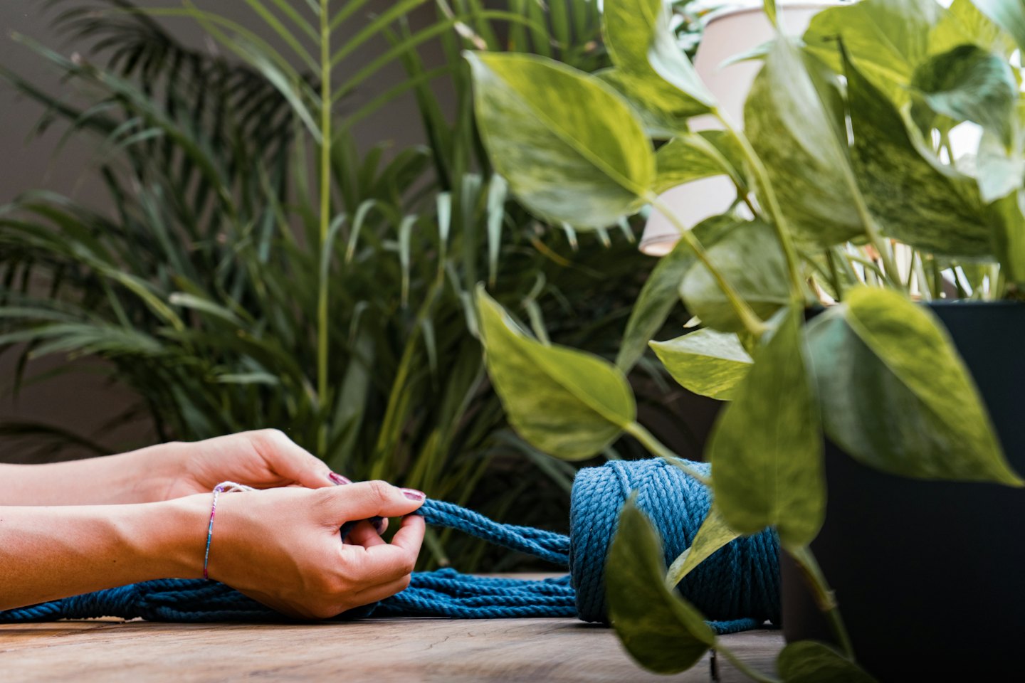 Hands knot blue macrame cord on a wooden table.